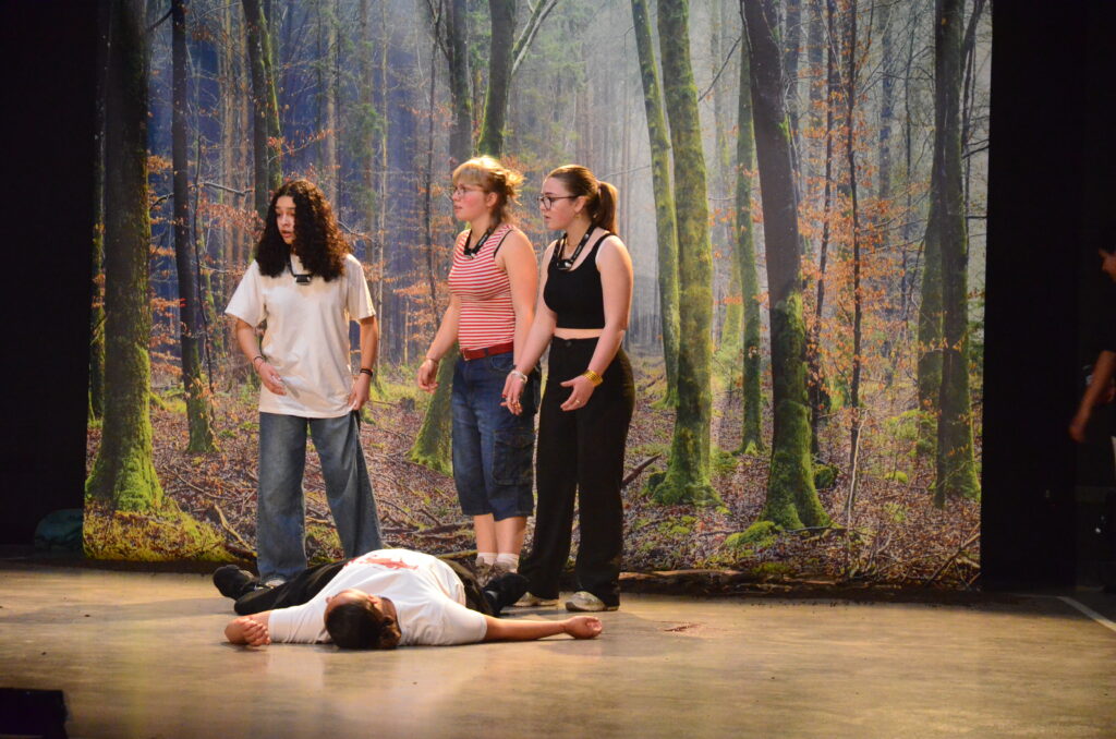 Trois personnages retrouvent l'un de leurs camarades inanimés et allongé par terre.